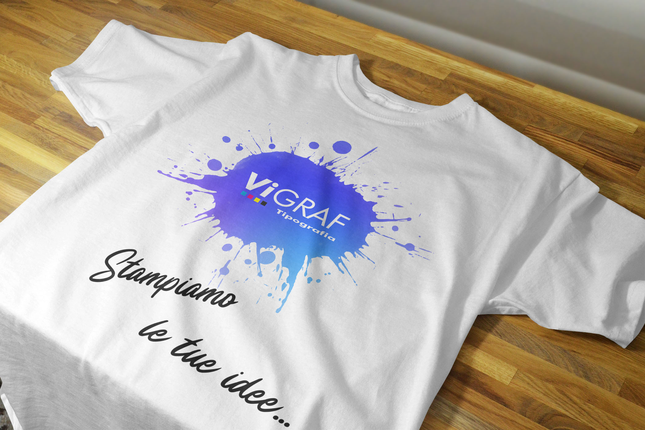 Dettaglio di t-shirt bianca con logo Vigraf a effetto schizzo blu e scritta "Stampiamo le tue idee"