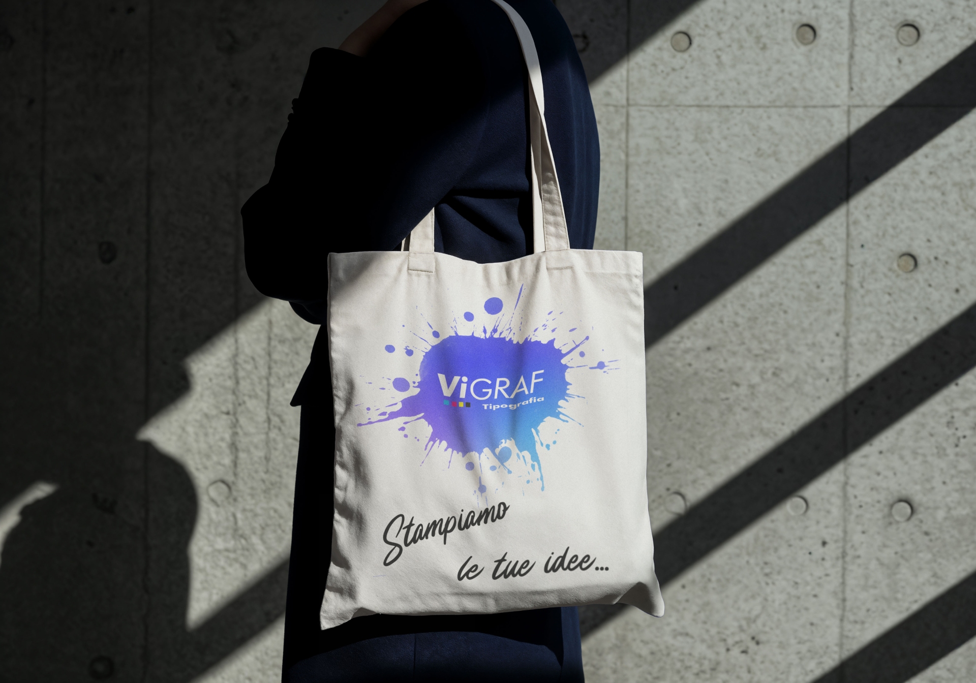 Tote bag naturale indossata a spalla con logo Vigraf a effetto schizzo blu e scritta "Stampiamo le tue idee"