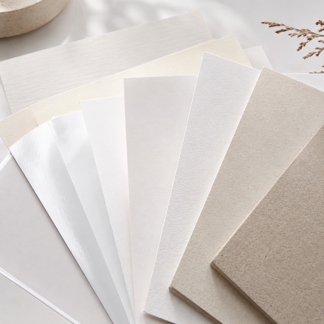 Campionario di fogli di carta di diverse texture e tonalitÃ , dal bianco al beige, disposti a ventaglio